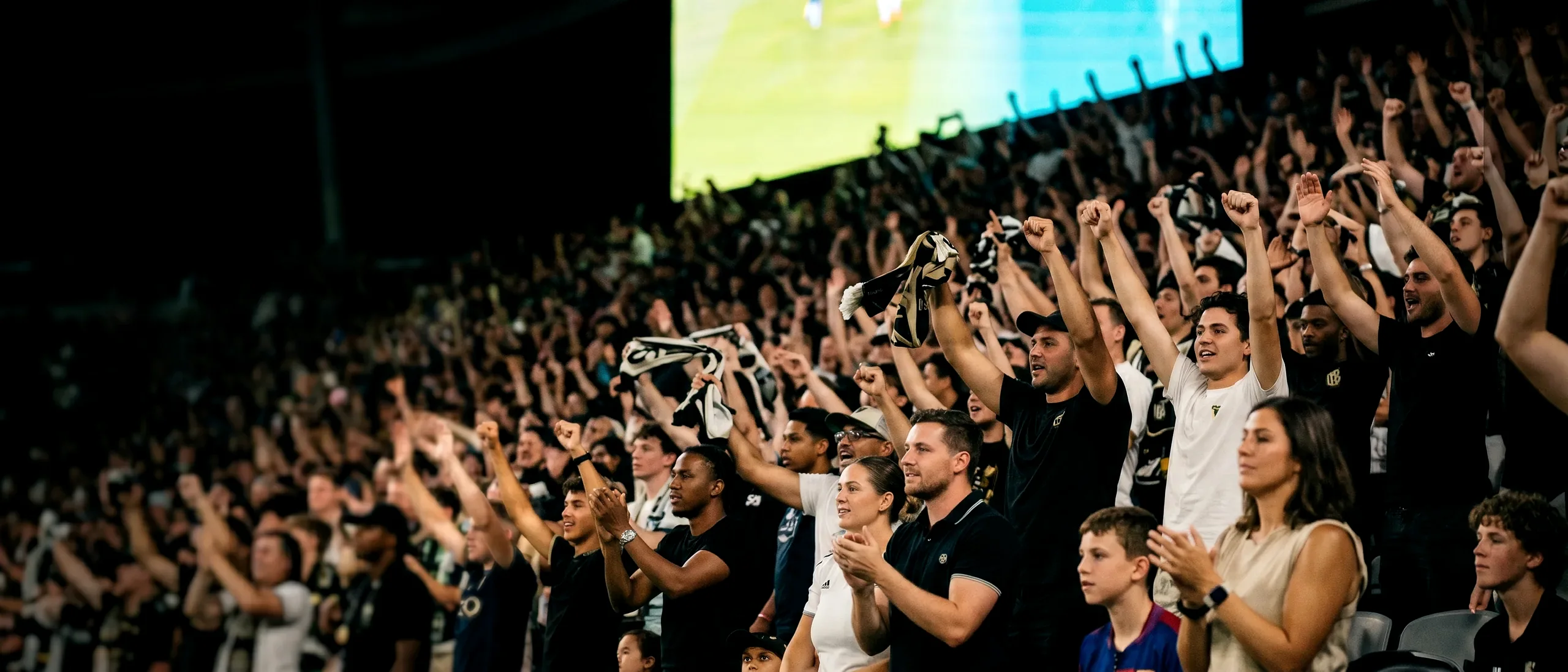 A packed stadium crowd at night cheering, scarves raised